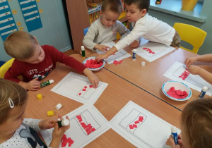 Kilkoro dzieci przy stoliku wykleja kontur flagi Polski kawałkami czerwonego papieru.